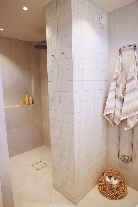 Stilren duschpelare med vit vertikal mosaik och naturstensgolv